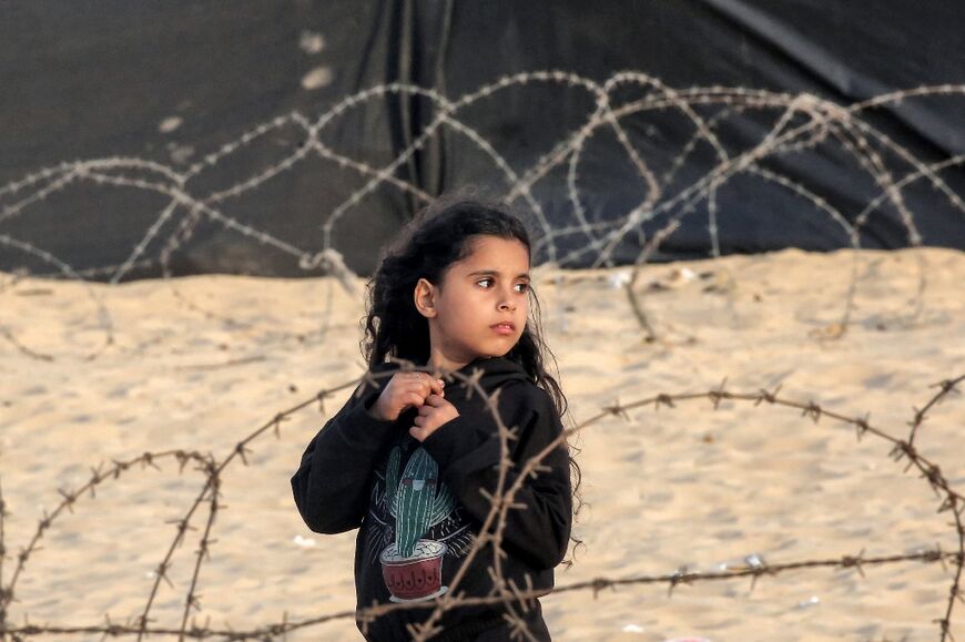 A girl stands behind barbed wire at a camp for displaced Palestinians in Rafah in the southern Gaza Strip on April 30, 2024
