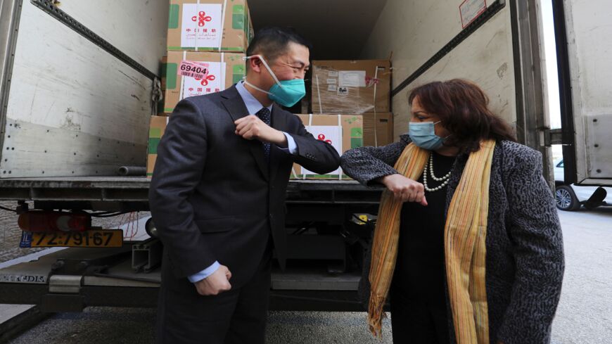 Chinese Ambassador Guo Wei (L) and Palestinian Health Minister Mai al-Kaila bump elbows during the unloading of a shipment of the Sinopharm COVID-19 vaccines donated by the Chinese government in the city of Ramallah in the West Bank, on March 29, 2021.