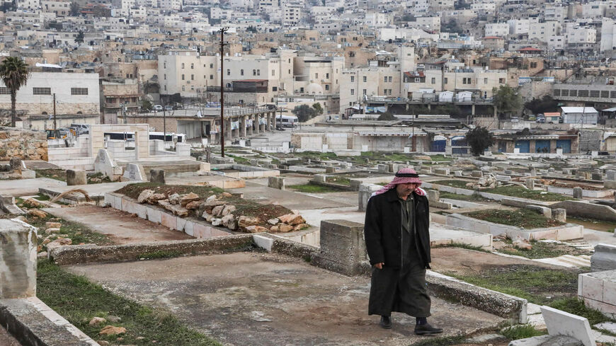 An elderly Palestinian walks through a cemetery in Hebron, with in the background an old market building along al-Shuhada Street that was designated by Israel to be a new settlement, with existing settler buildings behind, West Bank, Jan. 28, 2020.