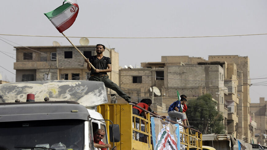 A Syrian man holds the Iranian flag as a convoy carrying aid provided by Iran arrives in Deir ez-Zor, Syria, Sept. 20, 2017.