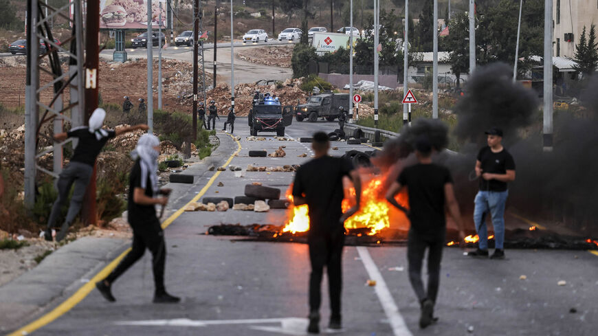 Palestinian youths stand behind a makeshift barricade of flaming tires separating them from Israeli security forces during clashes at the northern entrance of the city of Ramallah, West Bank, Oct. 3, 2022.