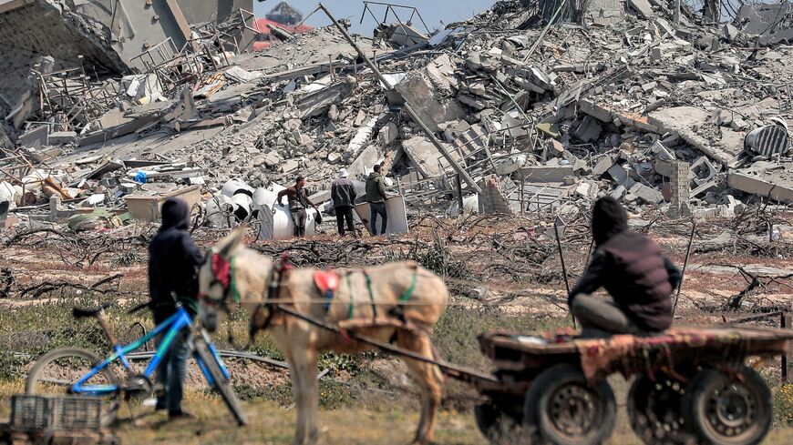 A person sits on a donkey-drawn cart while watching from a far as people search the rubble of destroyed buildings in the Asra residential compound.