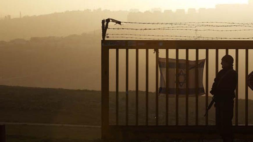 An Israeli soldier stands guard near a gate at the main entrance to the unauthorized Jewish outpost of Migron near the West Bank city of Ramallah February 8, 2012. Migron perches high on a blustery hill in the occupied West Bank. Its inhabitants pay taxes, are hooked up to the electricity grid and get round-the-clock protection from Israeli soldiers. Over the past decade the government has spent at least 4 million shekels ($1.1 million) on establishing and maintaining the cluster of squat, prefab bungalows,