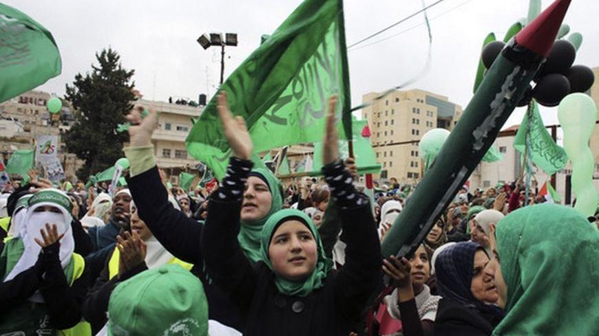A supporter holds a model of a Hamas-made rocket as others wave flags during a rally in the West Bank city of Hebron, marking the 25th anniversary of the founding of Hamas, December 14, 2012. It was one of the first rallies Western-backed Palestinian President Mahmoud Abbas allowed to take place in the West Bank since 2007, when his Islamist rivals Hamas seized control of the Gaza Strip. REUTERS/Ammar Awad (WEST BANK - Tags: POLITICS ANNIVERSARY)