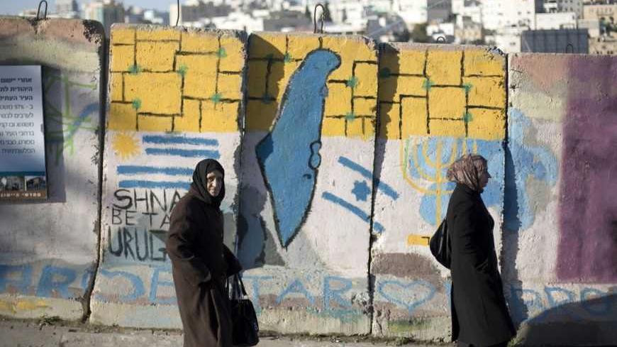 Palestinians walk past a blast wall with graffiti in the West Bank city of Hebron January 13, 2013. Entrenched in what they view as their Biblical heartland, the hardline Jewish settlers of Hebron look forward with delight to next week's Israeli election. Picture taken January 13, 2013. To match ISRAEL-ELECTION/SETTLERS   REUTERS/Baz Ratner  (WEST BANK - Tags: POLITICS ELECTIONS)