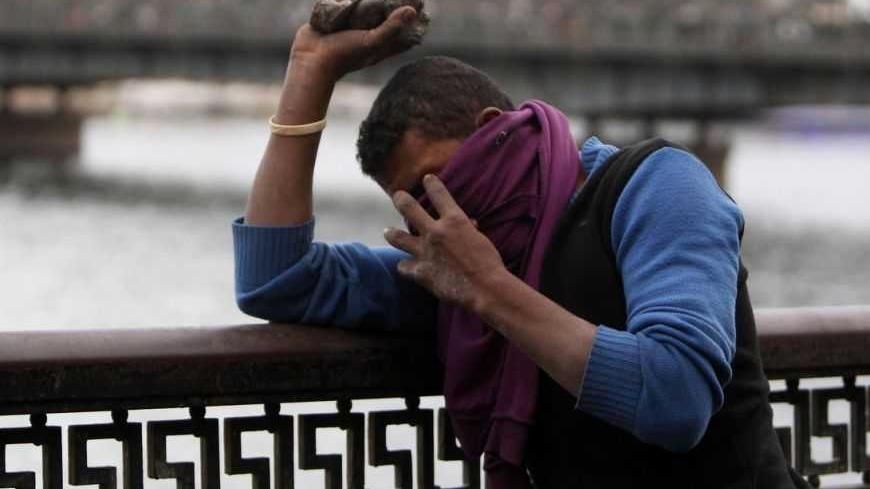 A protester opposing Egyptian President Mohamed Mursi covers his face from tear gas fired by riot police during clashes along Qasr Al Nil bridge, which leads to Tahrir Square, in Cairo January 28, 2013. A man was shot dead on Monday in a fifth day of violence that has killed 50 Egyptians and prompted the Islamist president to declare a state of emergency in an attempt to end a wave of unrest sweeping the biggest Arab nation.      REUTERS/Mohamed Abd El Ghany   (EGYPT - Tags: POLITICS CIVIL UNREST) - RTR3D3K