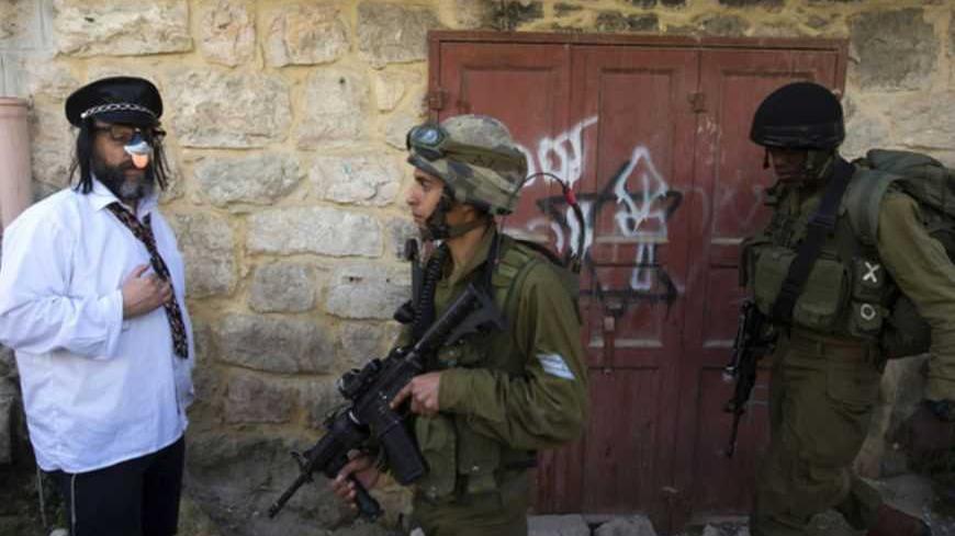 A Jewish settler, dressed in costume, stands near Israeli soldiers as they guard a parade for the holiday of Purim in the West Bank city of Hebron February 24, 2013. Purim is a celebration of the Jews' salvation from genocide in ancient Persia, as recounted in the Book of Esther. REUTERS/Ronen Zvulun (WEST BANK - Tags: SOCIETY RELIGION MILITARY TPX IMAGES OF THE DAY) - RTR3E7ED
