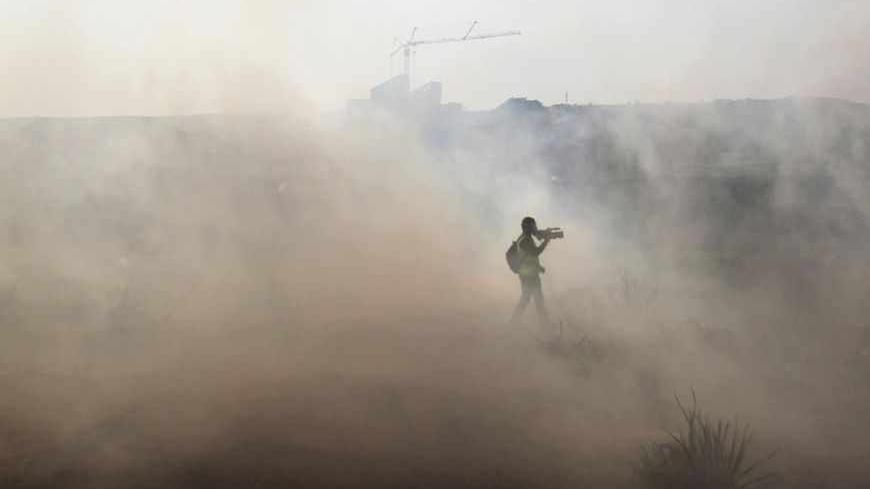 A journalist walks through tear gas fired by Israeli security officers (unseen) during clashes with stone-throwing Palestinians following a rally marking the 48th anniversary of the founding of the Fatah movement, in the West Bank village of Bilin near Ramallah January 4, 2013. REUTERS/Ammar Awad (WEST BANK - Tags: POLITICS CIVIL UNREST) - RTR3C3NU