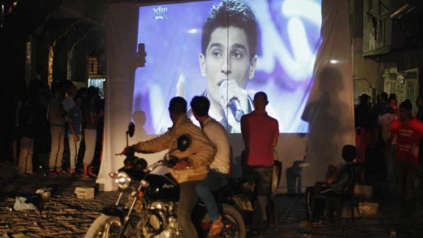 People watch Palestinian singer Mohammed Assaf as he sings in Beirut during the "Arab Idol" program, in Khan Younis in the southern Gaza Strip June 22, 2013. The 22-year-old singer Mohammed Assaf, from the Gaza Strip, was named the winner of "Arab Idol" in a TV talent contest in Beirut.  REUTERS/Ibraheem Abu Mustafa (GAZA - Tags: SOCIETY ENTERTAINMENT) - RTX10XJ1