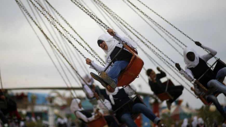 Palestinian girls sit on a carousel inside an amusement park built on the land of a former Israeli settlement in central Gaza Strip, April 11, 2013. REUTERS/Mohammed Salem (GAZA - Tags: SOCIETY) - RTXYHFP