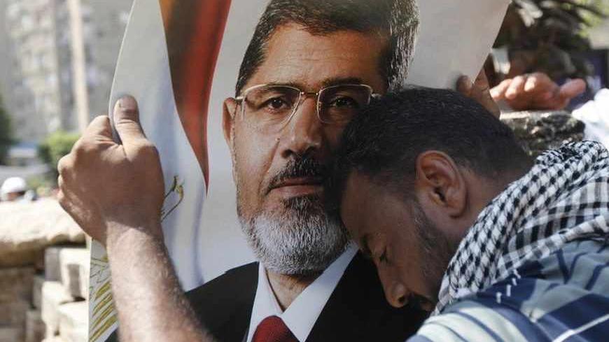 A protester supporting deposed Egypt's President Mohamed Mursi holds a poster of Mursi during clashes outside the Republican Guard barracks where Mursi is being held in Cairo July 5, 2013. At least three protesters were shot dead on Friday outside the barracks in Cairo, security sources said, as angry Islamist supporters confronted troops across the country. REUTERS/Mohamed Abd El Ghany (EGYPT - Tags: POLITICS CIVIL UNREST) - RTX11DTC