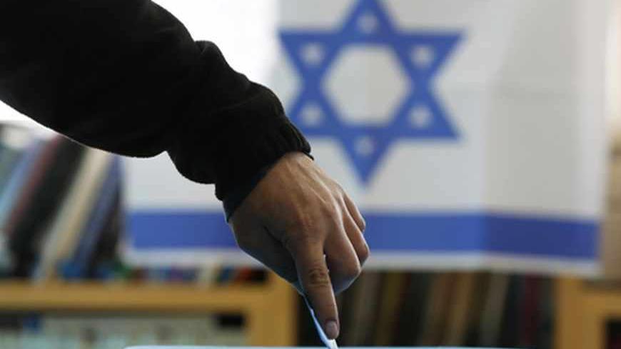 An Israeli flag is seen in the background as a man casts his ballot for the parliamentary election at a polling in the West Bank Jewish settlement of Ofra, north of Ramallah January 22, 2013. Israelis voted on Tuesday in an election that is expected to see Prime Minister Benjamin Netanyahu win a third term in office, pushing the Jewish state further to the right, away from peace with the Palestinians and towards a showdown with Iran. REUTERS/Baz Ratner (WEST BANK - Tags: POLITICS ELECTIONS TPX IMAGES OF THE