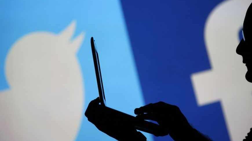 A man is silhouetted against a video screen with a Twitter and a Facebook logo as he poses with an Dell laptop in this photo illustration taken in the central Bosnian town of Zenica, August 14, 2013. REUTERS/Dado Ruvic (BOSNIA AND HERZEGOVINA - Tags: BUSINESS TELECOMS) - RTX12L7W