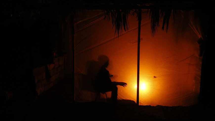 A Palestinian man warms himself by a fire inside his makeshift shelter during a power cut in the northern Gaza Strip November 11, 2013. Gaza's lone power plant shut its generators on November 1, 2013 due to a fuel shortage, a move that will likely increase already long blackout hours in the impoverished coastal territory run by the Islamist Hamas group. Power has been provided to different areas in the territory in six-hour shifts since the closure. REUTERS/Mohammed Salem (GAZA - Tags: ENERGY) - RTX159HC