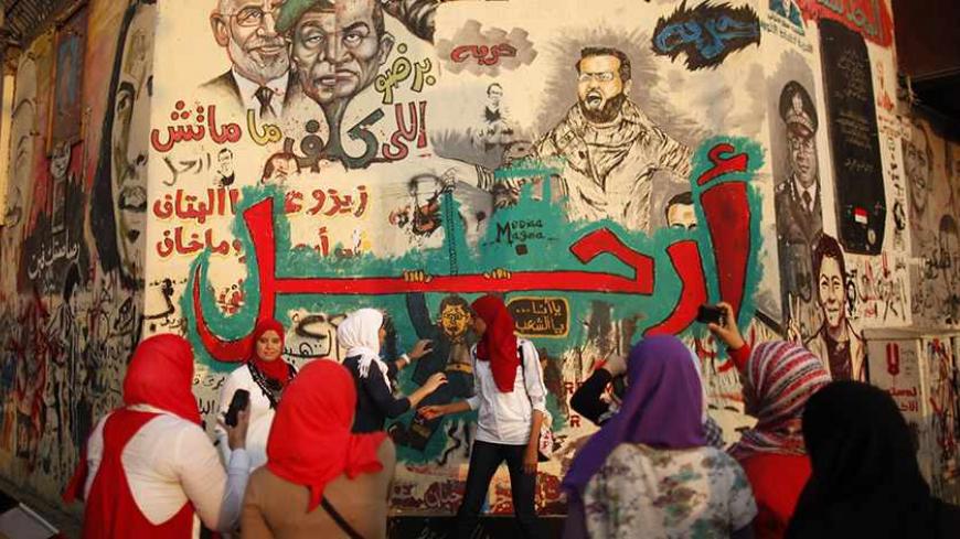 Women take pictures next to graffiti at Tahrir square in Cairo July 4, 2013. The writing reads: "Leave!" REUTERS/Khaled Abdullah (EGYPT - Tags: POLITICS CIVIL UNREST) - RTX11CRG