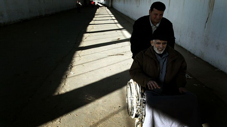 A PORTER PUSHES AN ELDERLY PALESTINIAN CANCER PATIENT THROUGH THE EREZ CROSSING BETWEEN THE GAZA STRIP AND ISRAEL.  A porter pushes an elderly Palestinian cancer patient through the Erez crossing between the Gaza Strip and Israel March 21, 2004. Palestinian doctors complain Israel has stopped allowing ambulances to bring patients into Israel from Gaza, forcing the sick to cross unaided through the heavily guarded checkpoint. REUTERS/Goran Tomasevic - RTRFRM5