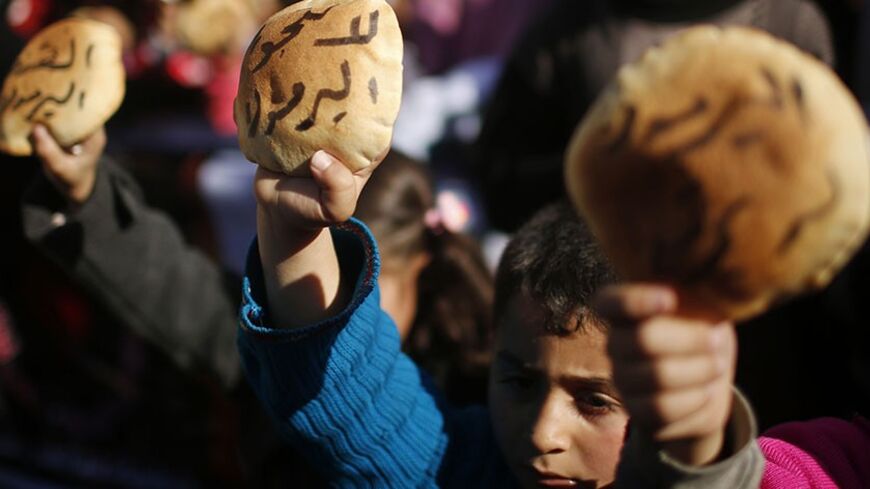 Palestinian children hold bread as they take part in a rally to show solidarity with Palestinian refugees in Syria's main refugee camp Yarmouk, in Gaza City January 16, 2014. The Arabic words on the bread read: "No to starving Yarmouk"  REUTERS/Mohammed Salem (GAZA - Tags: POLITICS CIVIL UNREST) - RTX17G3P