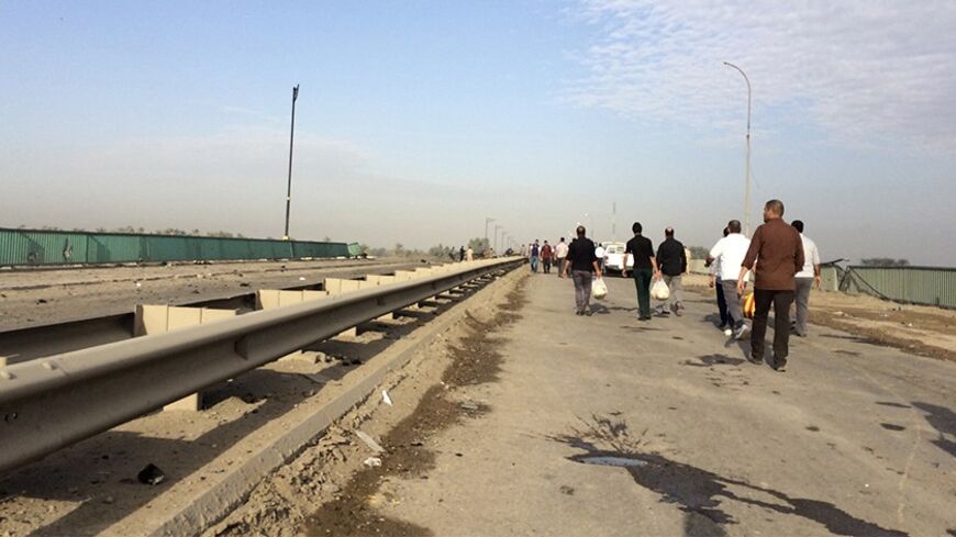 People walk past the site of Tuesday's car bomb attack on al-Muthna bridge at Taji, north of Baghdad March 26, 2014. At least nine people were killed and 25 others wounded when a suicide bomber drove a truck packed with explosives to an army checkpoint late Tuesday, police said. REUTERS/Ahmed Saad (IRAQ - Tags: CIVIL UNREST POLITICS) - RTR3IMQG