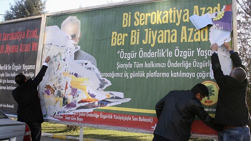 Plainclothes police officers tear down a billboard with a picture of imprisoned Kurdish rebel leader Abdullah Ocalan in Diyarbakir February 11, 2014. The face of jailed Kurdish rebel chief Ocalan briefly beamed down from billboards in southeast Turkey until police tore down the posters, a mark of official unease over his enduring influence among Kurds as local elections loom. The slogan on the billboard reads in Turkish and Kurdish " With free leadership to free life". Picture taken February 11, 2014. To ma