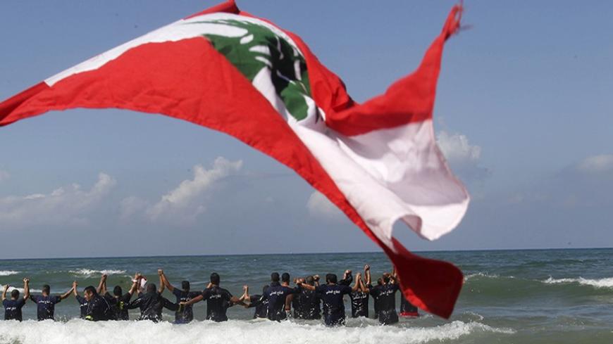Members of the Lebanese Civil Defence stand in the sea near a Lebanese flag during a protest in Beirut April 9, 2014. Workers from public sectors went on strike on Wednesday to demand more rights. REUTERS/Sharif Karim (LEBANON - Tags: POLITICS CIVIL UNREST) - RTR3KJCX