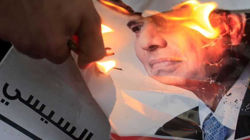 A demonstrator burns a poster of Egypt's former army chief Abdel Fattah al-Sisi during a protest against a law restricting demonstrations near El-Thadiya presidential palace in Cairo, April 26, 2014. REUTERS/Amr Abdallah Dalsh (EGYPT - Tags: POLITICS CIVIL UNREST) - RTR3MR3N