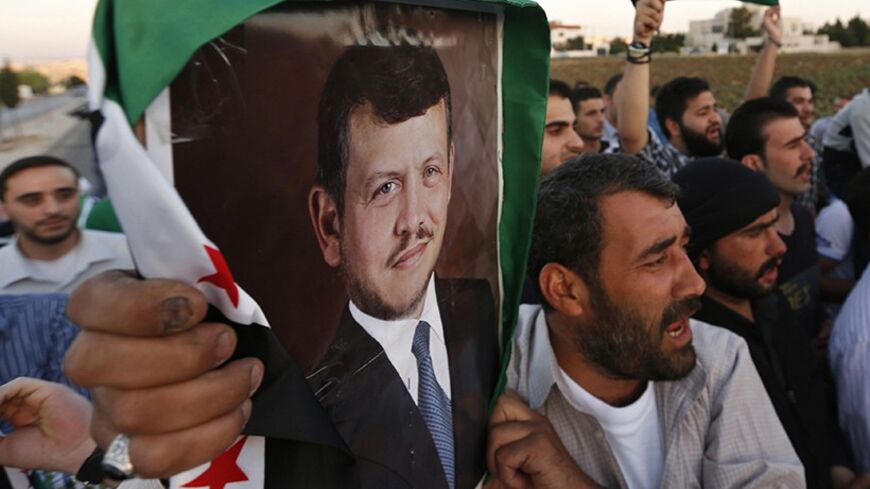 Syrians living in Jordan and Jordanian activists hold up the Syrian opposition flag alongside a picture of Jordan's King Abdullah, during a demonstration in front of the Syrian embassy in Amman May 26, 2014. Dozens of Syrian and Jordanian celebrated after Syria declared Jordan's charge d'affaires in Damascus persona non grata in response to what it said was an unjustified decision by the kingdom to expel its ambassador, Syrian state television said on Monday. REUTERS/Muhammad Hamed (JORDAN - Tags: POLITICS 