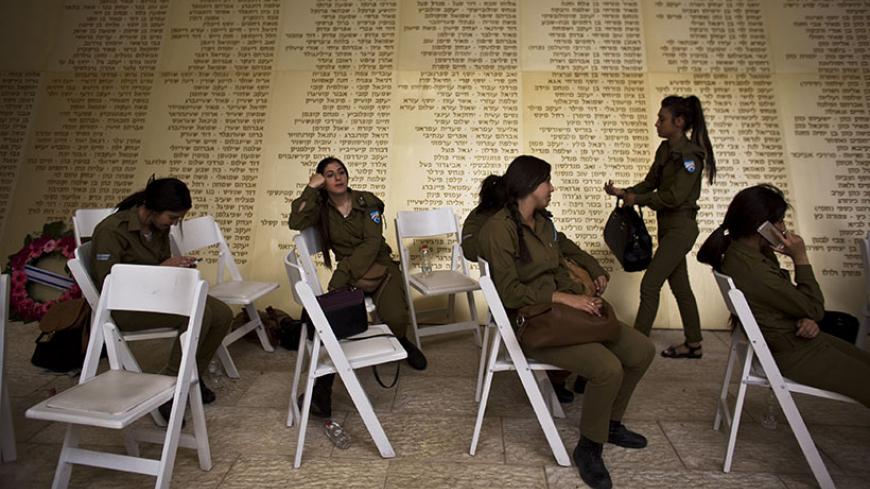 Israeli soldiers sit in front of a monument engraved with names of fallen Israeli soldiers, as they wait for the start of a ceremony marking Memorial Day in Jerusalem May 4, 2014. Israel commemorates its fallen soldiers on Memorial Day, which begins Sunday night. REUTERS/Nir Elias (JERUSALEM - Tags: ANNIVERSARY POLITICS CONFLICT TPX IMAGES OF THE DAY) - RTR3NQIS