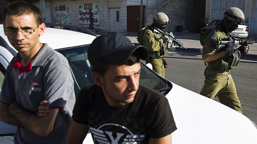 Palestinians lean against a car as Israeli soldiers take part in an operation to locate three Israeli teens in the West Bank City of Hebron June 17, 2014. Israel decided on Tuesday to widen a crackdown on Hamas in the West Bank after troops detained more than 40 members of the Palestinian Islamist group in sweeps conducted in tandem with a search for the three missing Jewish teenagers. REUTERS/Amir Cohen (WEST BANK - Tags: POLITICS MILITARY) - RTR3UAUQ