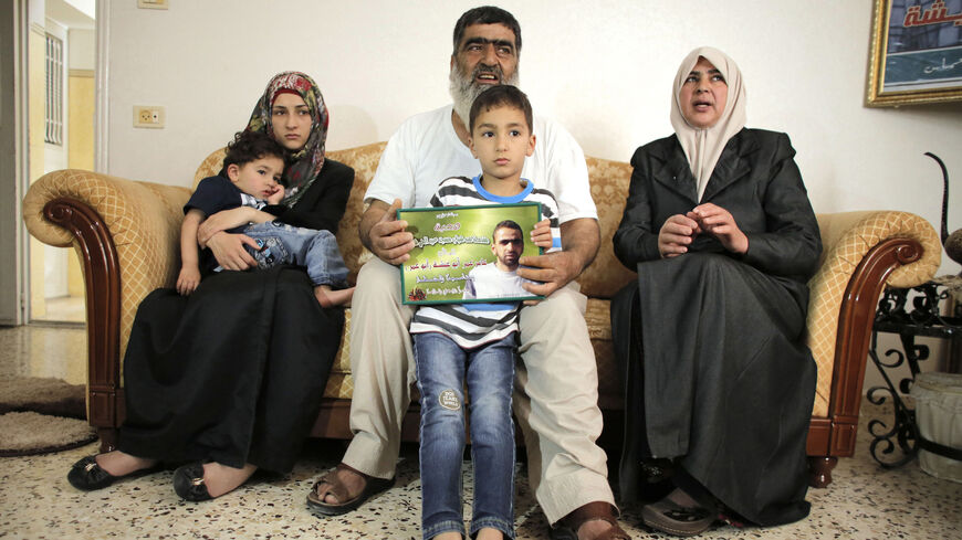 The son of Amer Abu Aysha holds his father's picture as he poses with his grandfather (C), grandmother (R) and his mother for media in their house in the West Bank city of Hebron June 27, 2014. Israel on Thursday named Abu Aysha as one of two leading suspects from a group of Hamas Islamists it suspects are behind the June 12 kidnappings of three Israeli teenagers, in the most concrete report yet of results after weeks of searches in the occupied West Bank. Israel's Shin Bet Security Agency said in a stateme