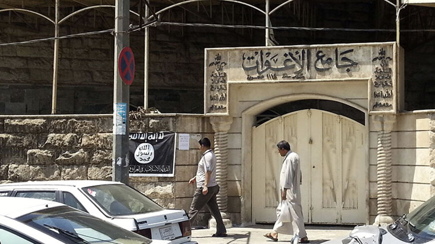 People walk past a banner (in black and white) belonging to the Islamic State in Iraq and the Levant (ISIL) in the city of Mosul, June 28, 2014. Since early June, ISIL militants have overrun most majority Sunni Muslim areas in the north and west of Iraq, capturing the biggest northern city Mosul and late dictator Saddam Hussein's hometown of Tikrit. The banner reads, "There is no God but God, and Mohammad is his messenger."  REUTERS/Stringer (IRAQ - Tags: CIVIL UNREST POLITICS) - RTR3W71S