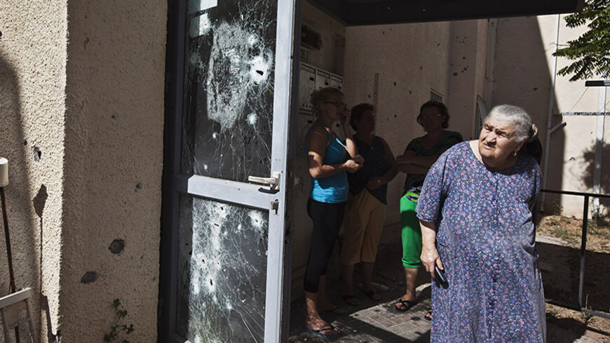 Israeli women stand near a building damaged after a rocket fired by Palestinian militants in Gaza landed in the southern town of Sderot July 15, 2014. Israel will intensify its week-old offensive against Hamas in Gaza, Prime Minister Benjamin Netanyahu said on Tuesday, after the Islamist group continued firing rockets at Israel instead of accepting an Egyptian-proposed ceasefire. REUTERS/Nir Elias (ISRAEL - Tags: POLITICS CIVIL UNREST) - RTR3YSAZ