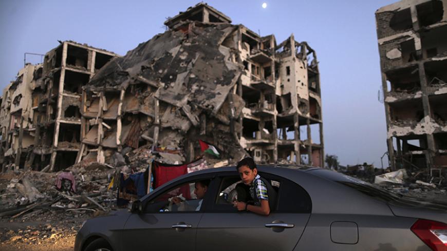 A Palestinian boy rides in a car driving past residential buildings in Beit Lahiya town, which witnesses said was heavily hit by Israeli shelling and air strikes during the Israeli offensive, in the northern Gaza Strip August 7, 2014. Mediators worked against the clock on Thursday to extend a Gaza truce between Israel and the Palestinians as the three-day ceasefire went into its final 24 hours. Israel has said it is ready to agree to an extension as Egyptian mediators pursued talks with Israelis and Palesti