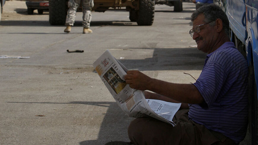 A motorist reads a newspaper on a street near a U.S. patrol passing by in Baghdad September 4, 2008.    REUTERS/Mohammed Ameen (IRAQ) - RTX8E9D