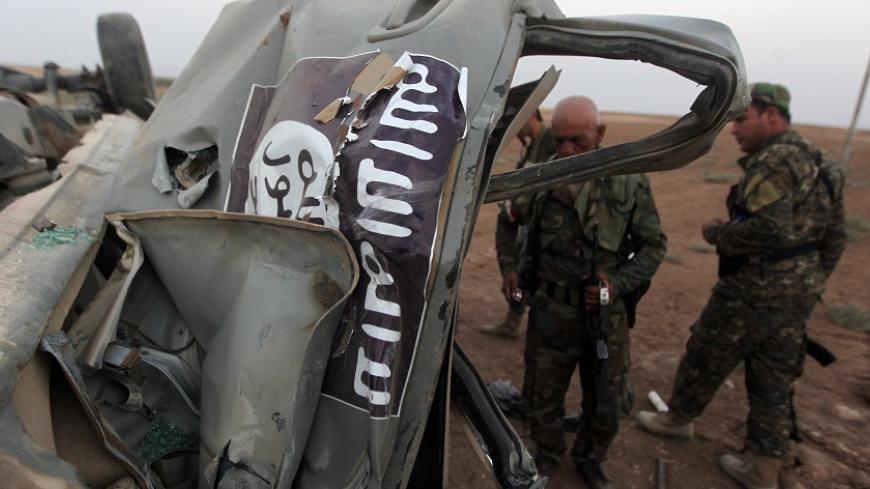 Peshmerga fighters inspect the remains of a car, bearing an image of the trademark jihadist flag, which belonged to Islamic State (IS) militants after it was targeted by an American air strike in the village of Baqufa, north of Mosul, on August 18,2014. Kurdish peshmerga fighters backed by federal forces and US warplanes pressed a counter-offensive Monday against jihadists after retaking Iraq's largest dam, as the United States and Britain stepped up their military involvement. AFP PHOTO/AHMAD AL-RUBAYE    