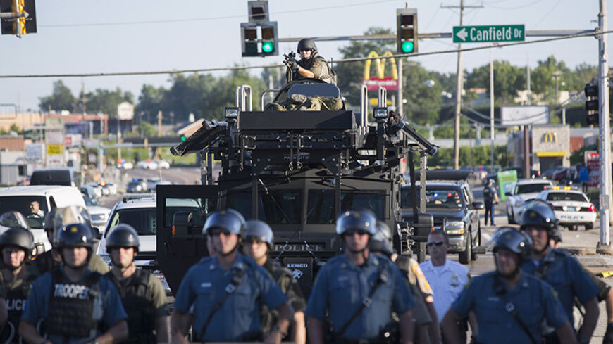 Riot police stand guard as demonstrators protest the shooting death of teenager Michael Brown in Ferguson, Missouri August 13, 2014. Police in Ferguson fired several rounds of tear gas to disperse protesters late on Wednesday, on the fourth night of demonstrations over the fatal shooting last weekend of an unarmed black teenager Brown, 18, by a police officer on Saturday after what police said was a struggle with a gun in a police car. A witness in the case told local media that Brown had raised his arms to