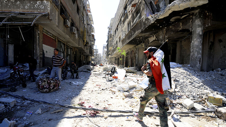 A member of forces loyal to Syria's President Bashar al-Assad holds the Syrian flag as he walks on debris of damaged buildings in al-Dukhaneya neighbourhood near Damascus, after the forces regained control of the area from rebel fighters October 7, 2014. REUTERS/Omar Sanadiki   (SYRIA - Tags: POLITICS CIVIL UNREST CONFLICT) - RTR499FJ