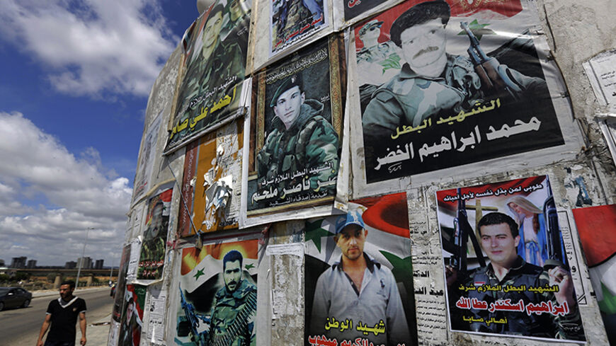 TO GO WITH AFP STORY BY SAMMY KETZ
A Syrian man walks past a wall bearing the portraits of soldiers from the city of Tartus, who died during the Syrian conflict, in the city northwest of Damascus on May 18, 2014. Tartus has itself largely escaped the conflict in Syria, but posters of its sons killed fighting for the regime elsewhere in the country line the western city's main road. AFP PHOTO/JOSEPH EID        (Photo credit should read JOSEPH EID/AFP/Getty Images)