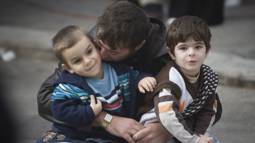 A man kisses his sons as he sits outside the Eyup Sultan mosque after Eid al-Fitr prayers in Istanbul September 20, 2009. REUTERS/Morteza Nikoubazl (TURKEY SOCIETY) - RTR2825L
