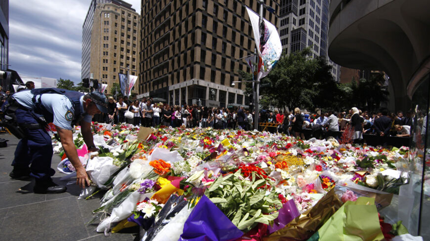 A policeman lays a floral tribute with thousands of others near the cafe where hostages were held for over 16-hours, in central Sydney December 16, 2014. Heavily armed Australian police stormed a Sydney cafe early on Tuesday morning and freed a number of hostages being held there at gunpoint, in a dramatic end to a 16-hour siege in which three people including the attacker were killed.  REUTERS/David Gray   (AUSTRALIA - Tags: CIVIL UNREST POLITICS) - RTR4I5JB