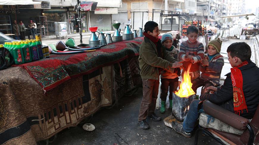Children warm themselves next to an open fire beside fuel barrels, engine oil and accessories displayed for sale in Aleppo January 13, 2015. Residents of Kafr Hamra, a town in the rural Aleppo countryside, refine crude oil in makeshift cottage refineries in warehouses and backyards for heating, operating bakeries and even running cars, just like most locals across rebel-held areas of Syria. The state no longer pumps gasoline to areas in rebel hands, and civilians have resorted to buying crude oil from armed