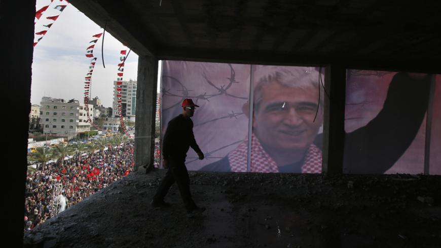 Palestinian walks past a poster depicting Ahmed Saadat, the jailed leader of the Popular Front for the Liberation of Palestine (PFLP), during a rally marking the 46th anniversary of the movement founding in Gaza City December 7, 2013. REUTERS/Suhaib Salem (GAZA - Tags: POLITICS CIVIL UNREST ANNIVERSARY) - RTX1680T