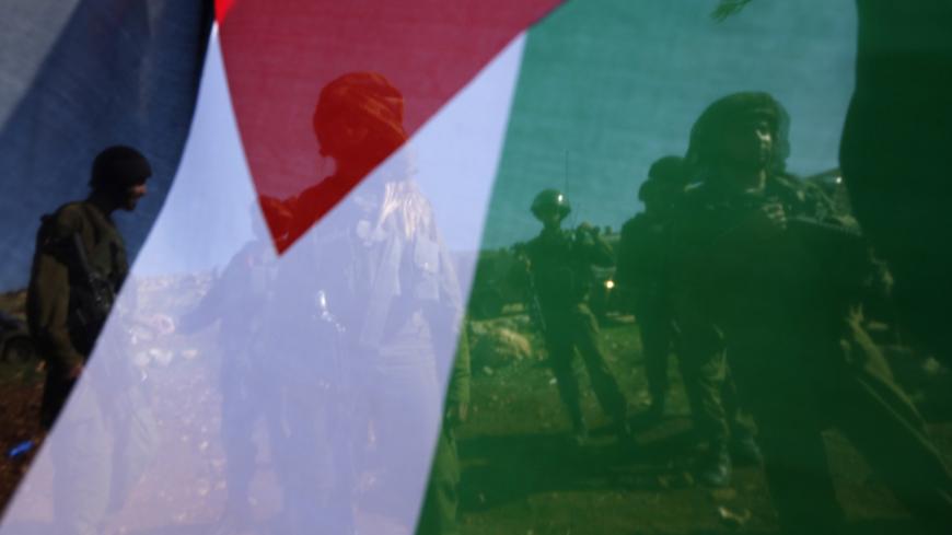 Israeli soldiers are pictured through a Palestinian flag as they stand guard during a protest by Palestinians against Jewish settlements near the West Bank city of Ramallah December 10, 2014. A Palestinian minister died on Wednesday shortly after an altercation with Israeli border police in the West Bank during which one of the policeman grabbed him by the neck. Ziad Abu Ein, 55, a minister without portfolio, was taking part in a protest against Israeli settlements when he was involved in clashes with aroun