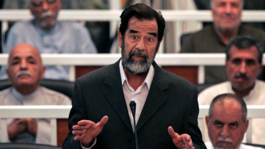 Saddam Hussein speaks to the Presiding Judge Rizgur Ameen Hana Al-Saedi as his trial begins in a heavily fortified courthouse in Baghdad's Green Zone October 19, 2005. Behind Saddam on his immediate right is Awad Hamad al-Badar, while in the second row are (R to L) Mizhar Abdullah Ruwayyid and Taha Yassin Ramadan. In the third row are (R to L) Ali Dayim Ali, Mohammed Azawi. A defiant Saddam went on trial on Wednesday for crimes against humanity over the killing of more than 140 Shi'ites more than two decade