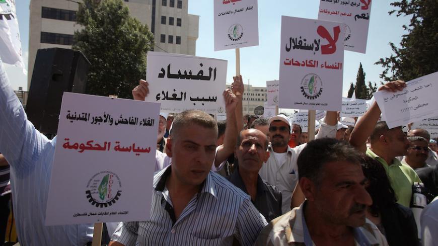 Palestinian protesters hold signs that read in Arabic "Corruption is the reason for high cost of living" and "High prices and low wages are the policies of the government" during a protest against the high cost of living in the West Bank city of Ramallah on September 11, 2012. Palestinain prime minister Salam Fayyad announced cuts to fuel prices and VAT after more than a week of protests across the West Bank over the spiralling cost of living. AFP PHOTO/ABBAS MOMANI        (Photo credit should read ABBAS MO