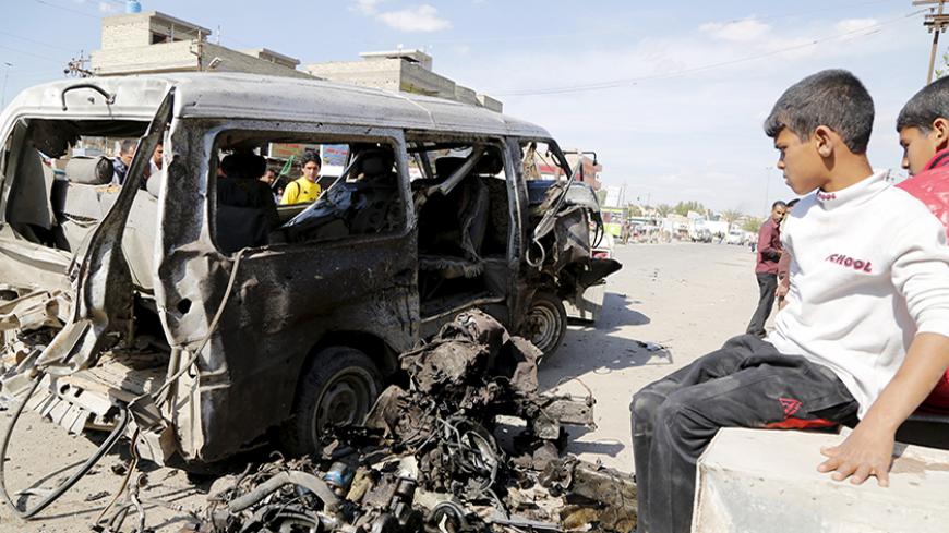 Boys look at a destroyed car at the site of a car bomb attack in Habibia district in Baghdad, March 23, 2015. The bomb killed two people and wounded 15, police and medics said. REUTERS/Wissm al-Okili  - RTR4UHTV
