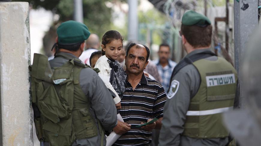 A Palestinian man carrying his daughter shows his identity card to Israeli border policemen as he makes his way with other Palestinians to attend the second Friday prayer of Ramadan in Jerusalem's al-Aqsa mosque,  at an Israeli checkpoint in the West bank city of Bethlehem June 26, 2015. REUTERS/Mussa Qawasma - RTX1HV74