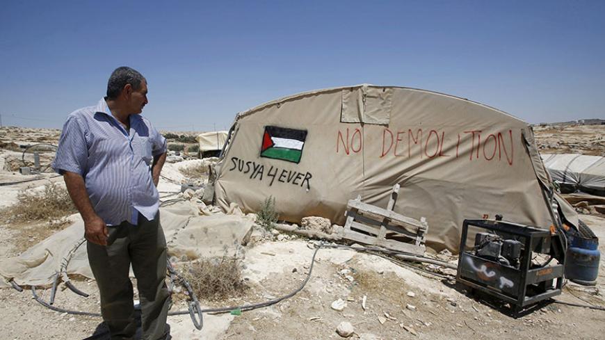 Palestinian man Jihad Nuwaja stands next to a tent in Susiya village, south of the West Bank city of Hebron July 20, 2015. Sitting under a fig tree to escape the searing sun, Nuwaja looks out on the only land he knows - the dry expanse of the Hebron hills in the southern West Bank. Within days, his home is set to be demolished and he, his wife and 10 children expelled.   REUTERS/Mussa Qawasma      TPX IMAGES OF THE DAY      - RTX1L1EB