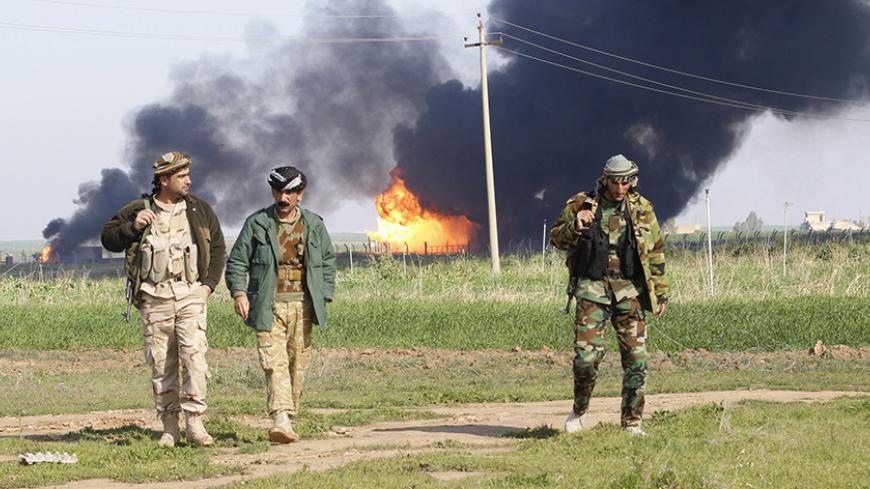 Smoke rises from the Khabbaz oilfield, behind Kurdish peshmerga forces, on the outskirts of Kirkuk, February 2, 2015. Production at the oilfield near the northern Iraq city of Kirkuk remained suspended on Monday after incurring severe damage during a weekend attack by Islamic State insurgents, Iraq's oil minister said.  REUTERS/Ako Rasheed (IRAQ - Tags - Tags: CIVIL UNREST CRIME LAW POLITICS ENERGY) - RTR4NWQ7