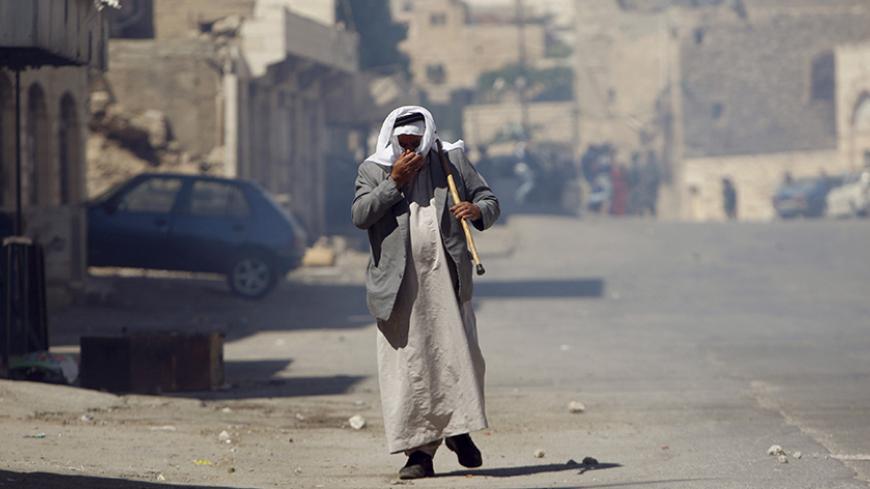 A Palestinian man covers his face from tear gas fired by Israeli troops during clashes following a protest against the Israeli police raid on Jerusalem's al-Aqsa mosque on Tuesday, in the occupied West Bank city of Hebron September 18, 2015. Israel deployed hundreds of extra police around the Old City of Jerusalem on Friday after Palestinian leaders called for a 'day of rage' to protest at new Israeli security measures. REUTERS/Mussa Qawasma - RTS1R5M
