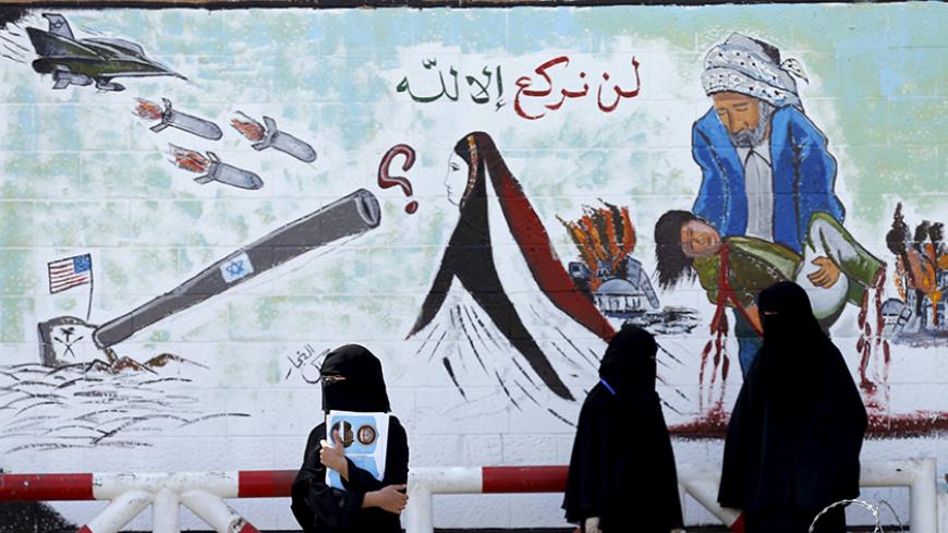 Women stand next a graffiti painted by pro-Houthi activists on the gate of the Saudi embassy in Yemen's capital Sanaa October 21, 2015. The writing reads, "We will kneel only to Allah". REUTERS/Khaled Abdullah - RTS5FPV